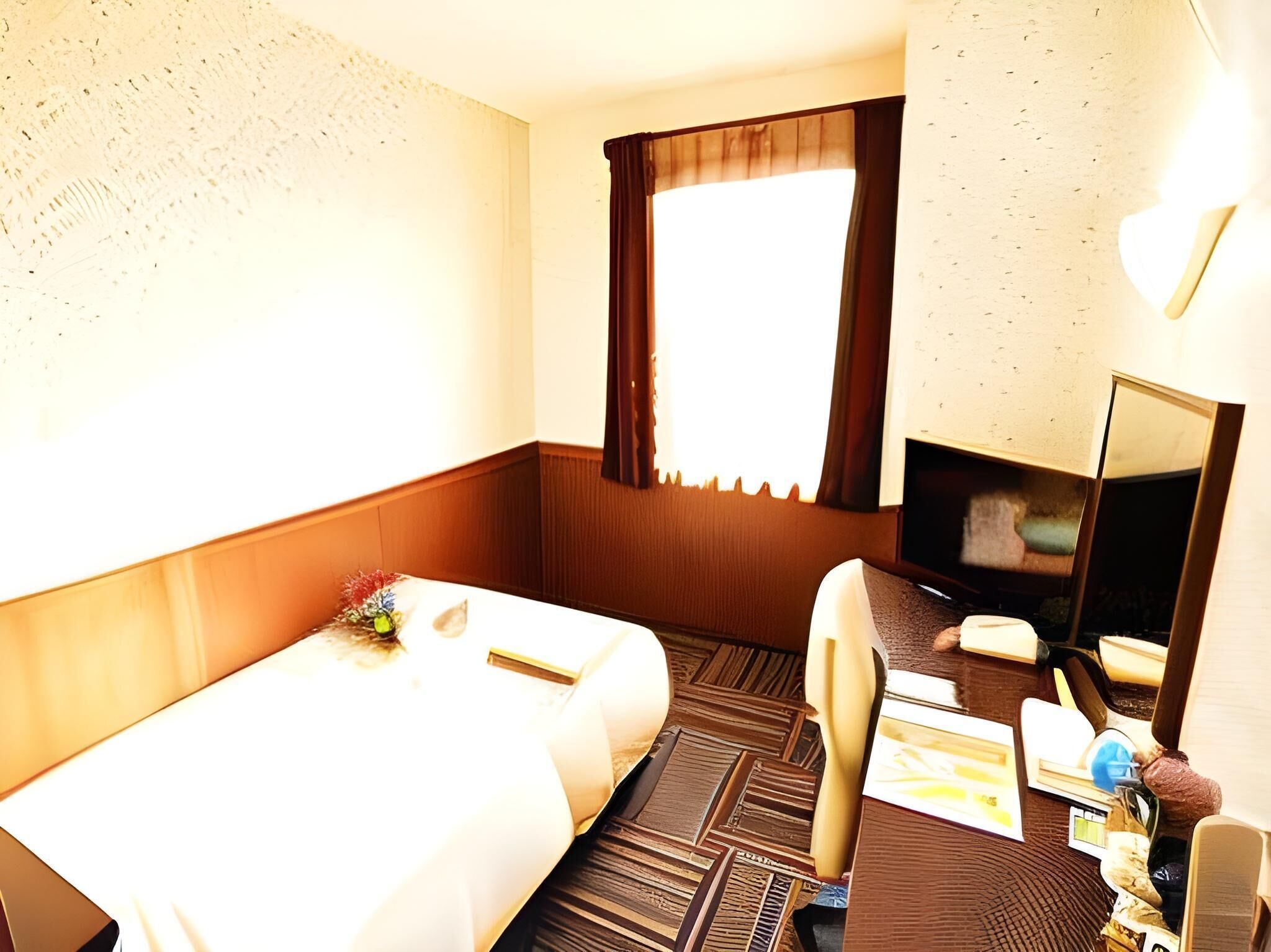 A hotel room with a bed, a desk, a chair, a television, and a window with curtains.