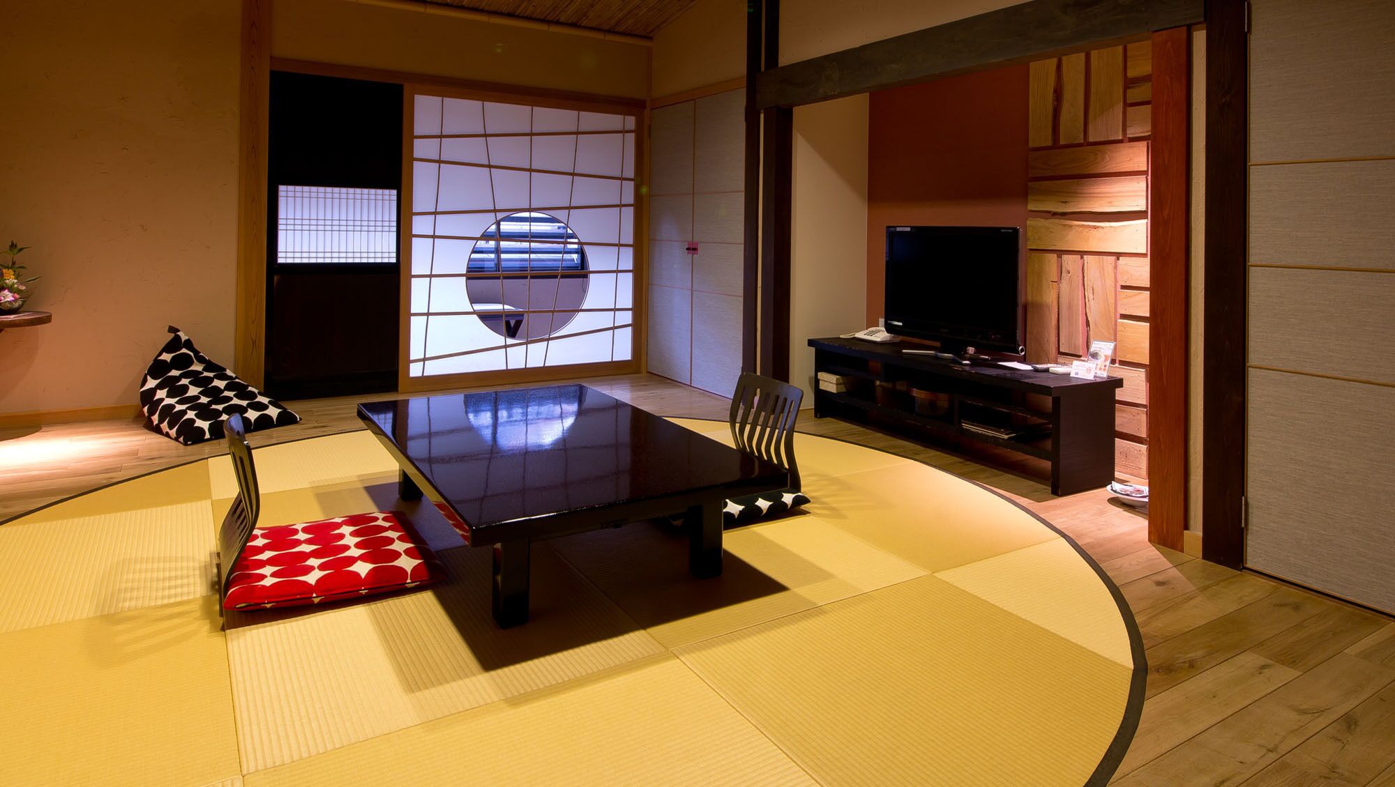 Ein traditioneller japanischer Raum mit Tatami-Böden, einem niedrigen Tisch, einem Fernseher und einer Schiebetür.