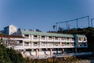 Un edificio de varios pisos con techo verde, múltiples balcones y una grúa de construcción al fondo.