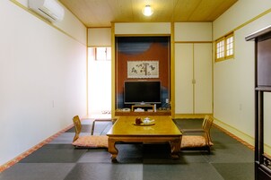 Una habitación tradicional japonesa con suelo de esteras de tatami, una mesa de madera baja y un televisor montado en la pared.