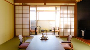 Um quarto japonês tradicional com tatames, uma mesa baixa com um conjunto de utensílios para chá e portas corrediças que dão para uma varanda.