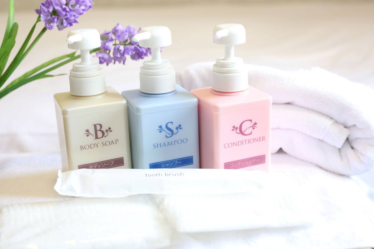 Tres botellas de productos de cuidado corporal: jabón de baño, champú y acondicionador, dispuestas sobre una toalla blanca junto a un cepillo de dientes.