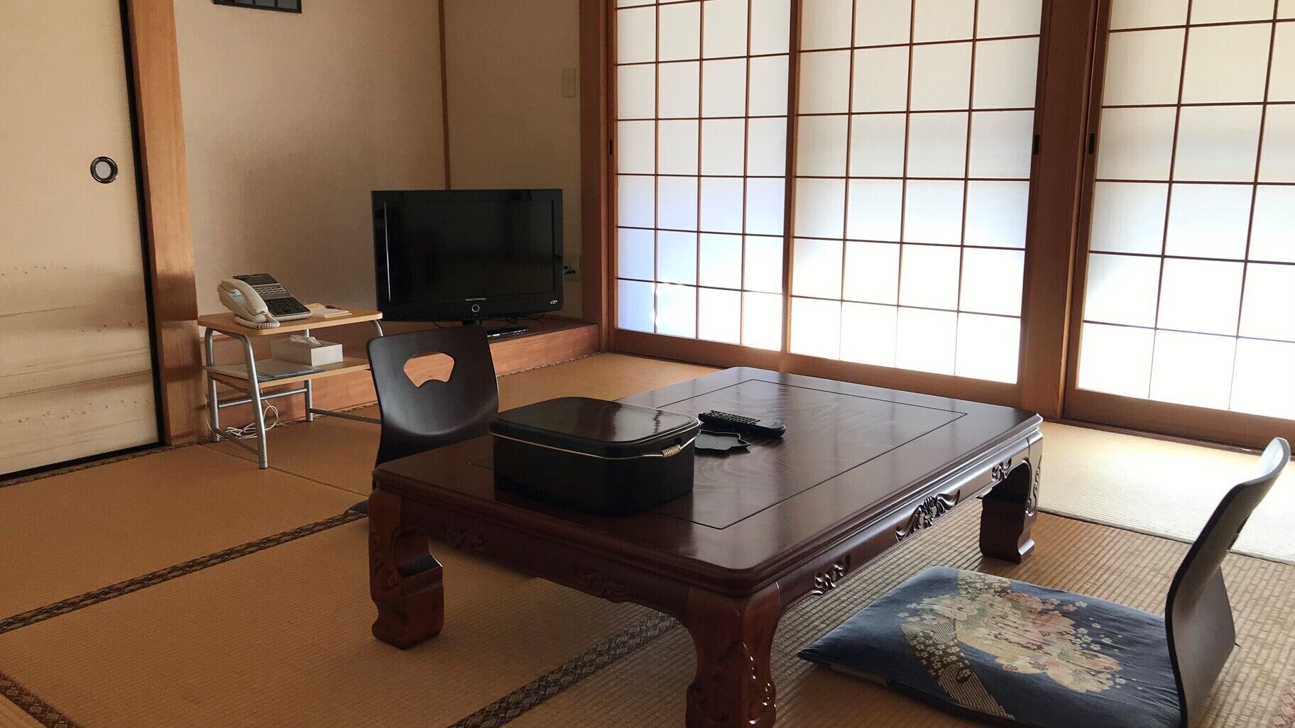 A traditional Japanese room with tatami flooring, a low table, a television, and a sliding shoji screen.