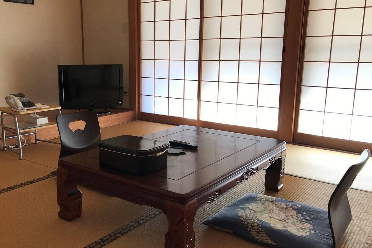 A traditional Japanese room with tatami flooring, a low table, a television, and a sliding shoji screen.