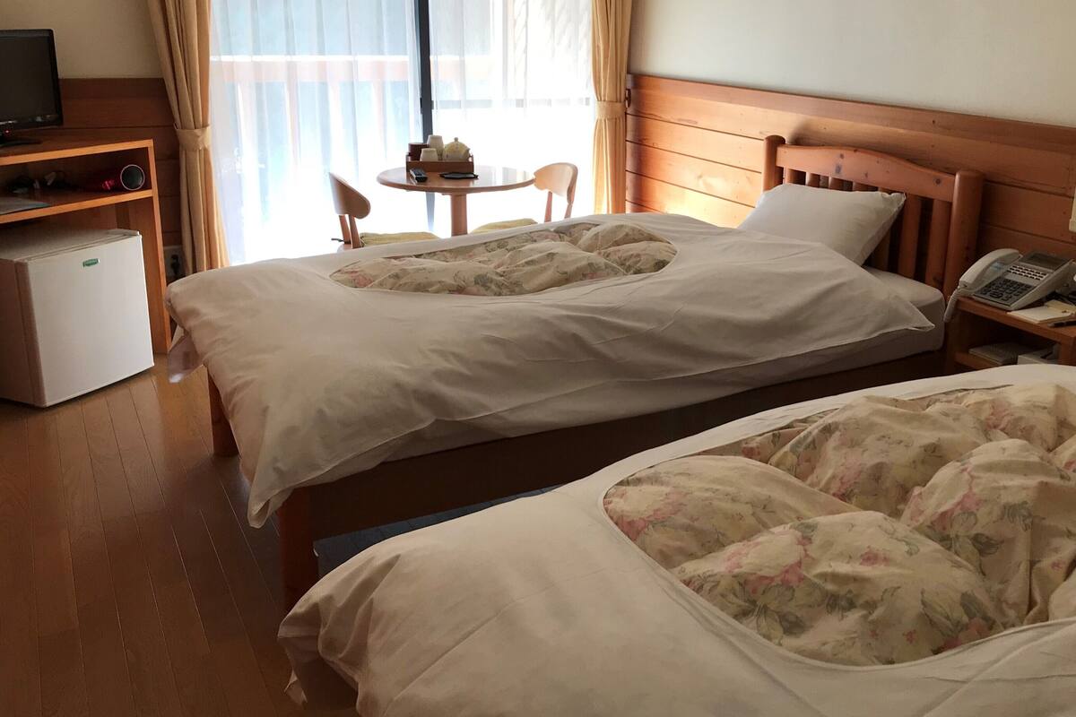 A hotel room with two beds, a desk with a computer, a chair, and a small refrigerator.