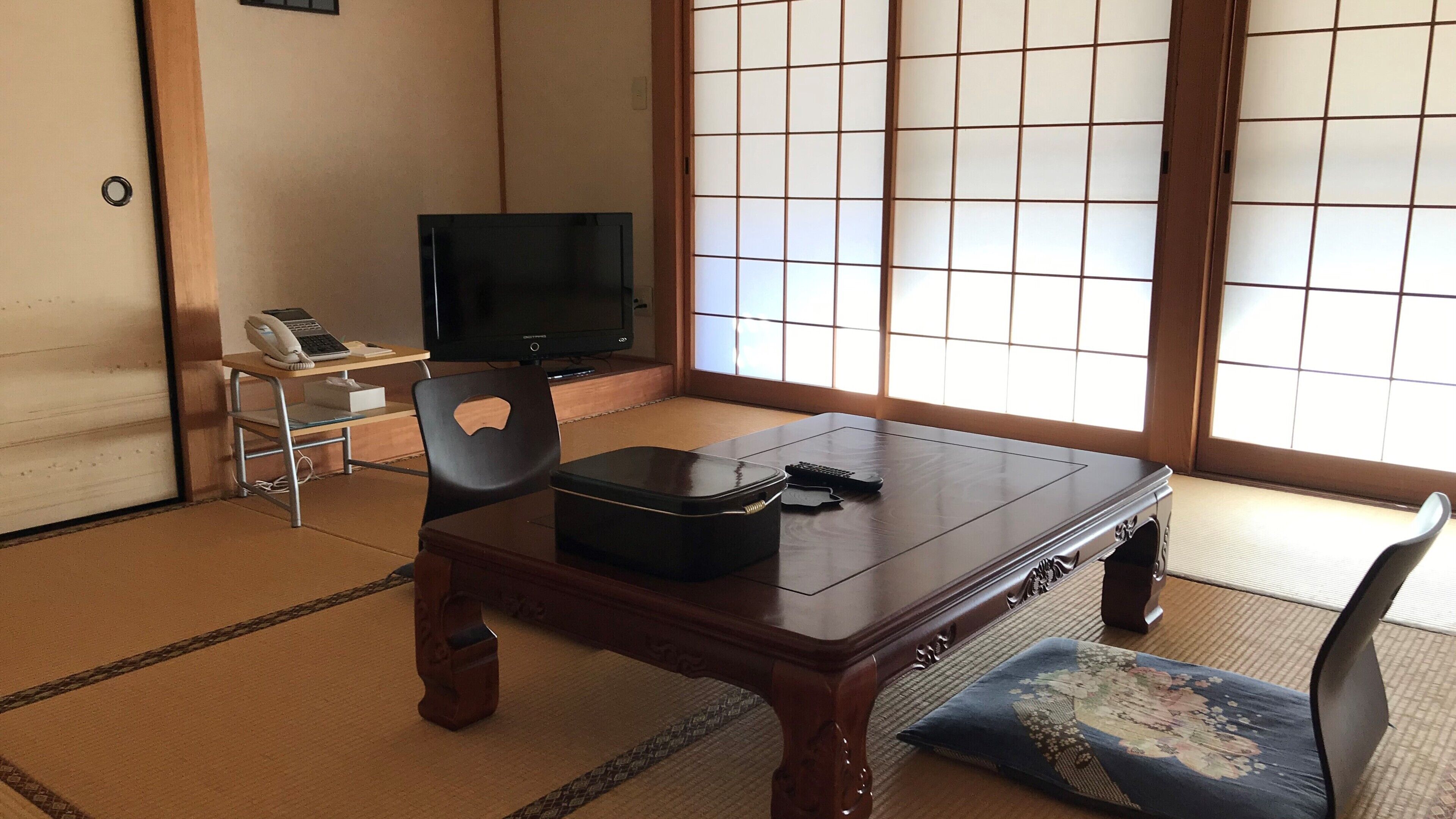 Una habitación japonesa tradicional con suelo de tatami, una mesa baja, un televisor y un divisor shoji.