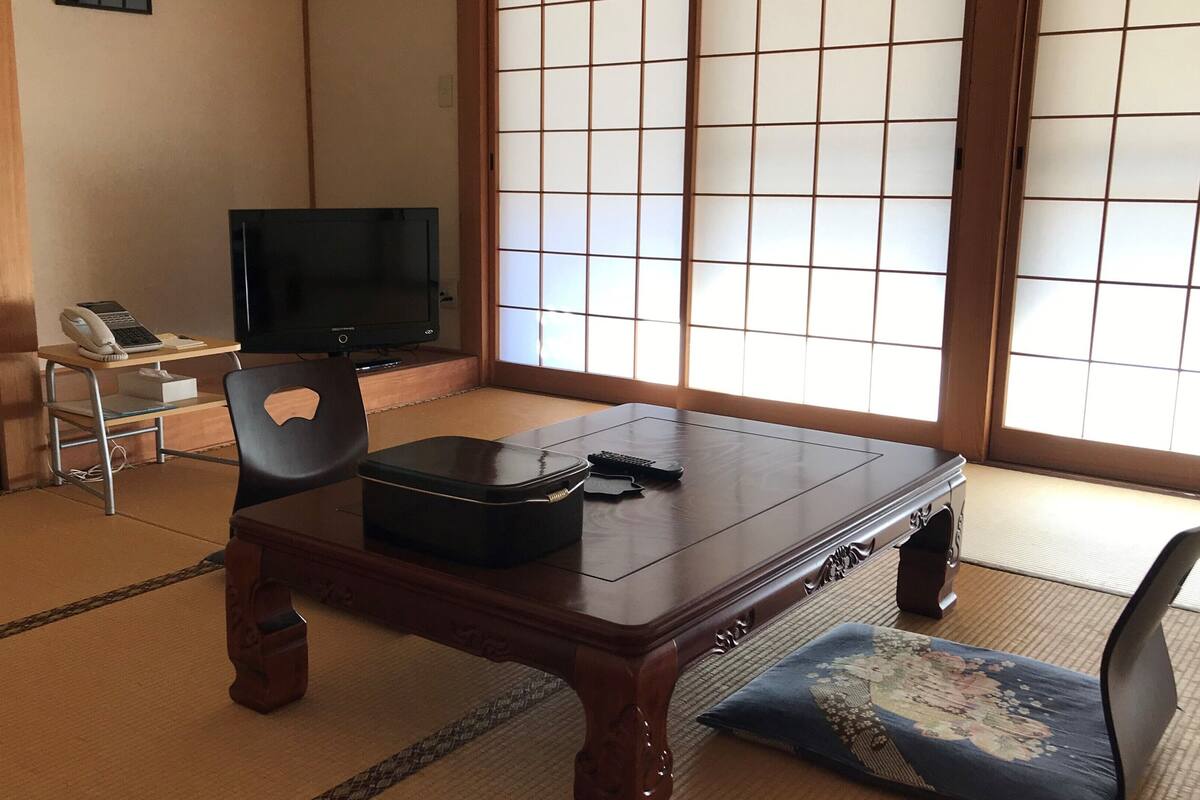 A traditional Japanese room with tatami flooring, a low table, a television, and a shoji screen.