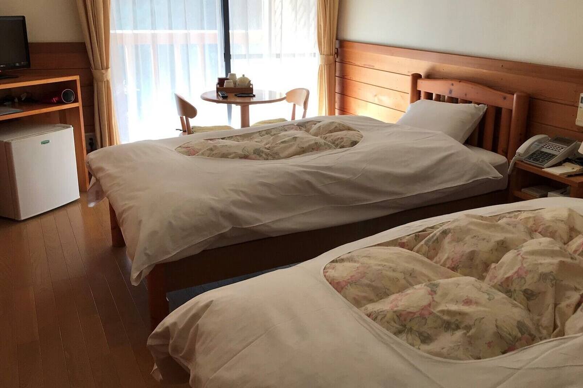 A hotel room with two beds, a desk with a computer, a chair, and a small refrigerator.