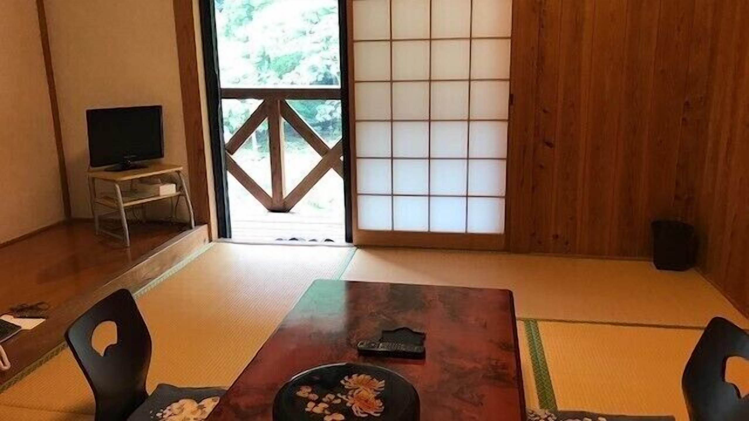 Una habitación japonesa tradicional con suelo de tatami, una mesa baja con un adorno y un fusuma con un diseño geométrico.