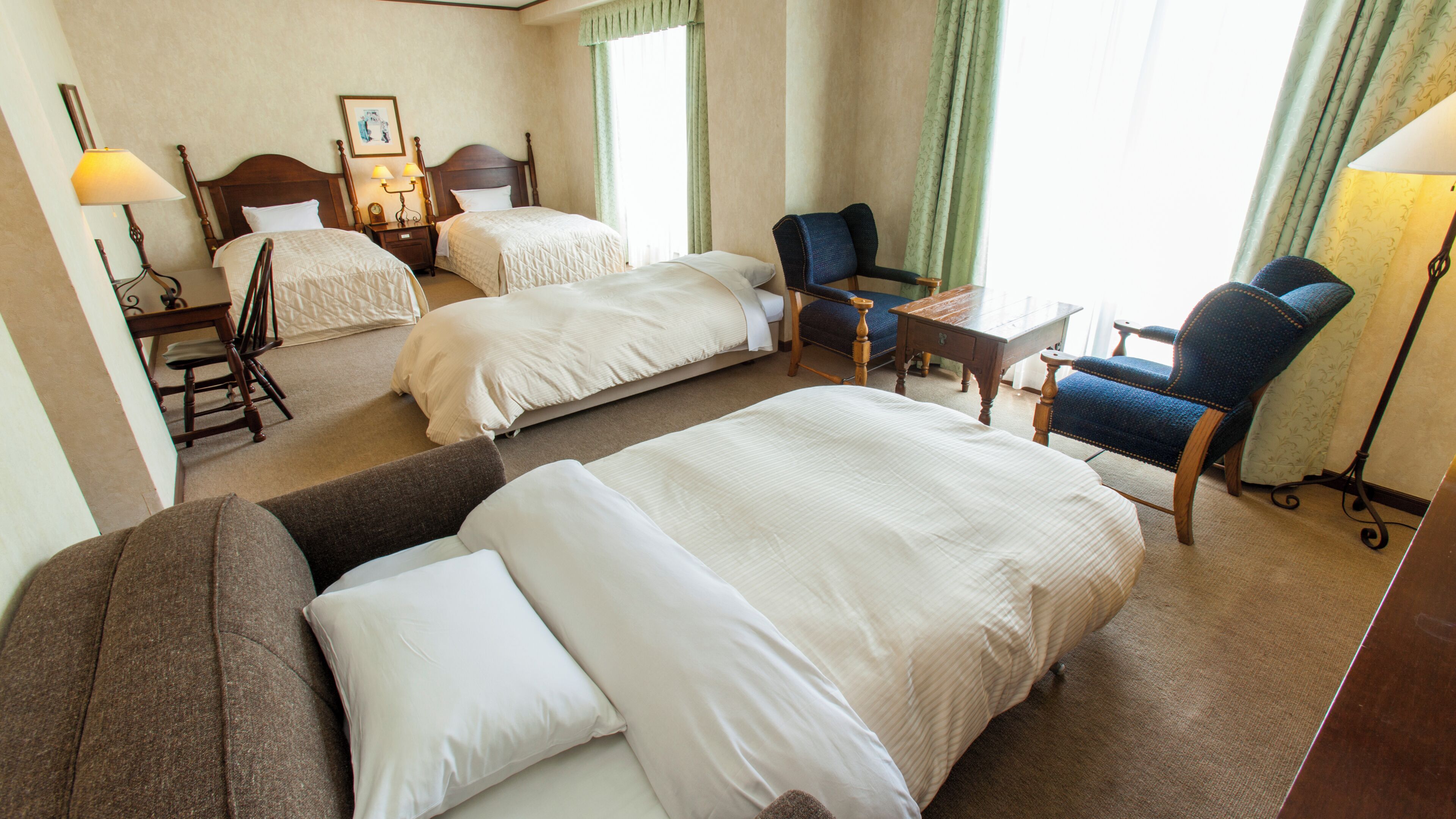 Quarto de hotel com duas camas, um sofá, uma poltrona, uma escrivaninha e um abajur.