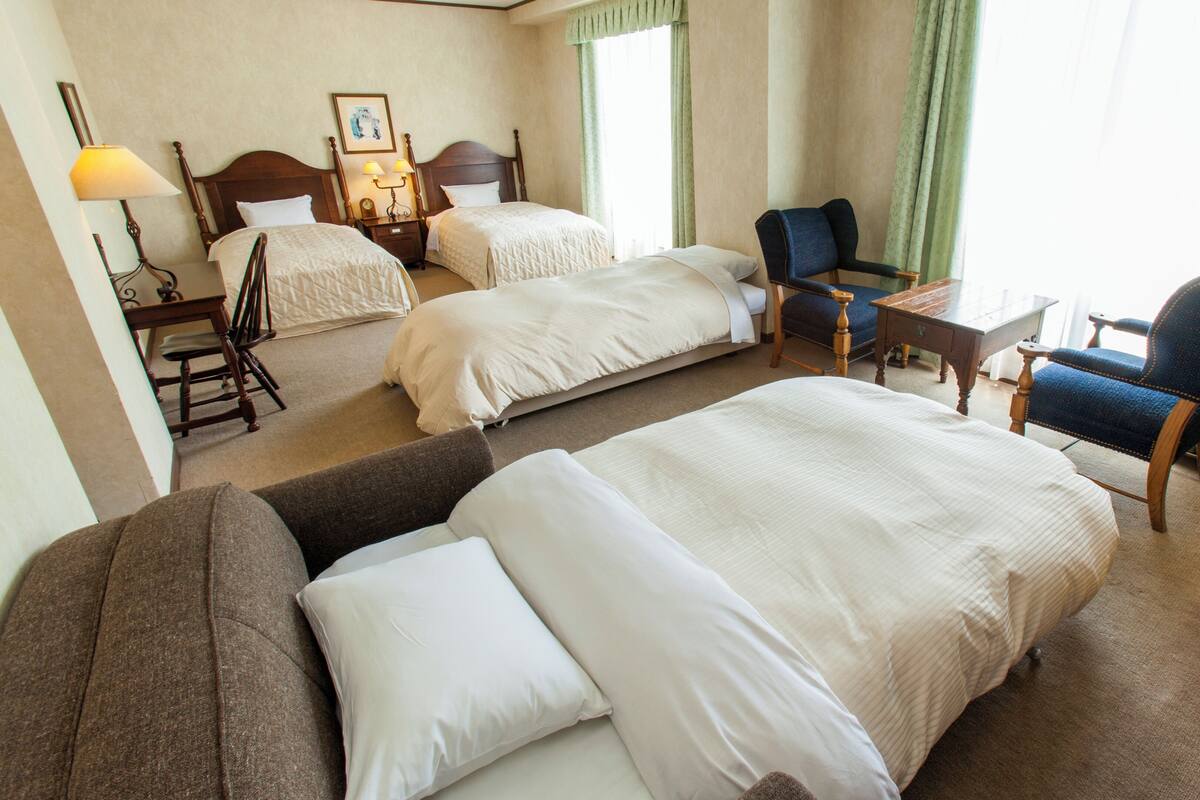 Habitación de hotel con dos camas, un sofá, una silla, un escritorio y una lámpara.