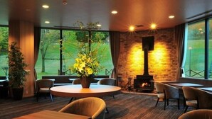 A modern interior with a round table, chairs, a fireplace, and large windows. - Kannabe Onsen Blue Ridge Hotel (TOYOKA SHI)