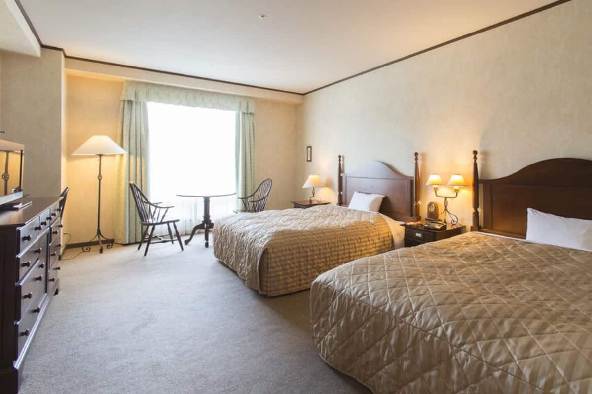 Una habitación de hotel con dos camas, un escritorio, una silla y una lámpara.