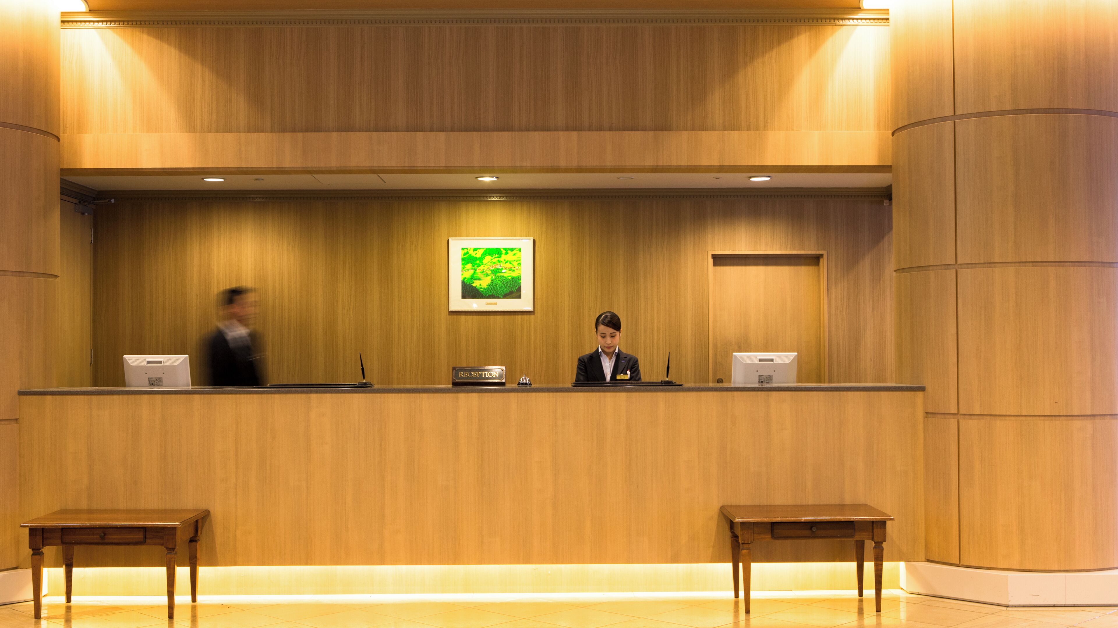 Una reception con un quadro incorniciato sopra, una targhetta e due piccoli tavolini antistanti.