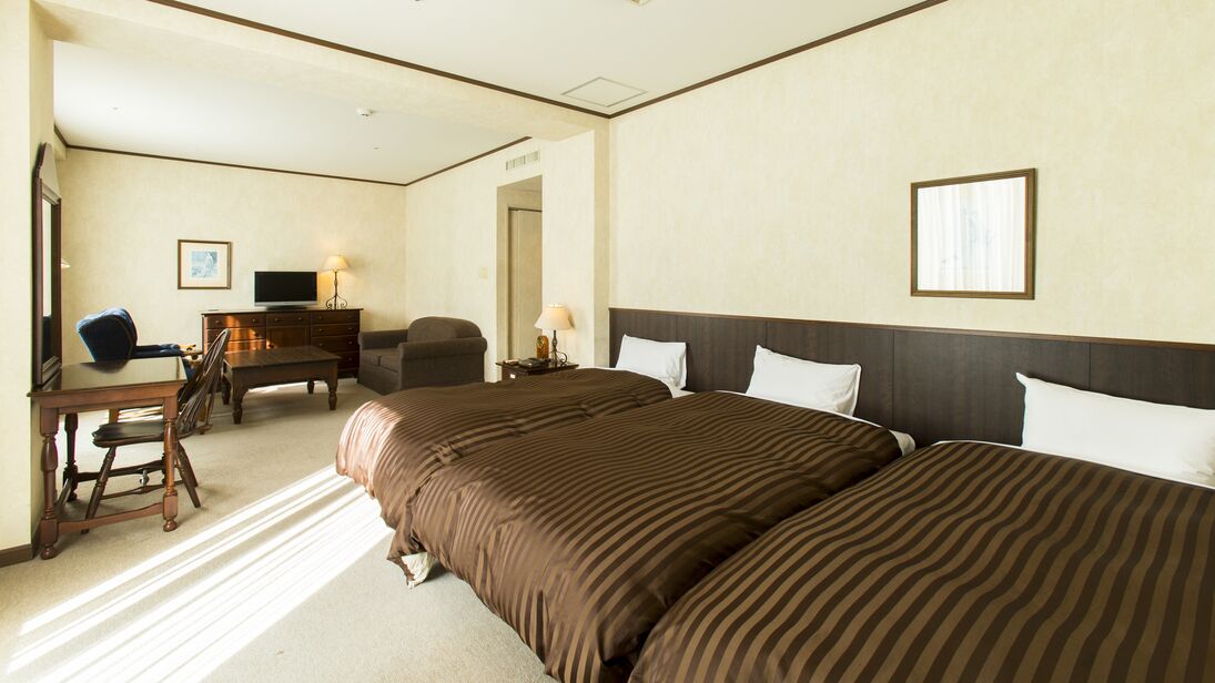 Quarto de hotel com uma cama grande, uma escrivaninha com cadeira, televisão e cómoda.