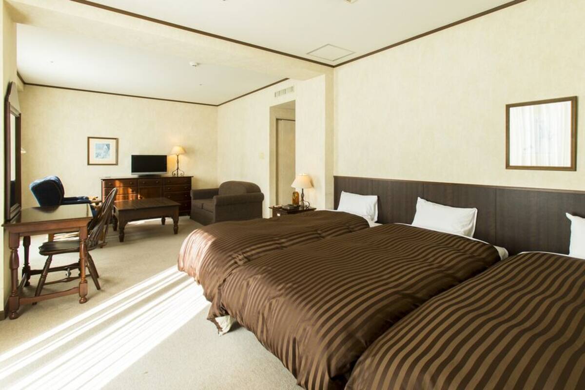 Habitación de hotel con una cama grande, un escritorio con una silla, televisión y cómoda.