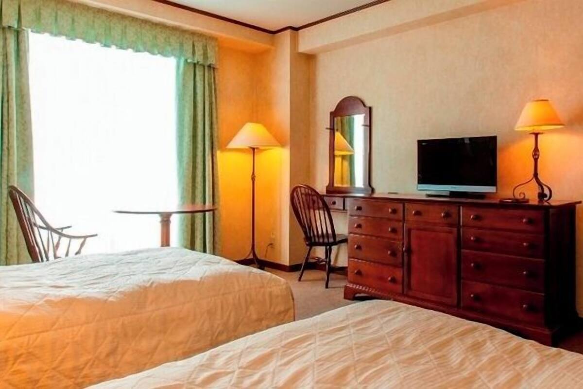 Habitación de hotel con dos camas, televisión, cómoda, una silla y un espejo.