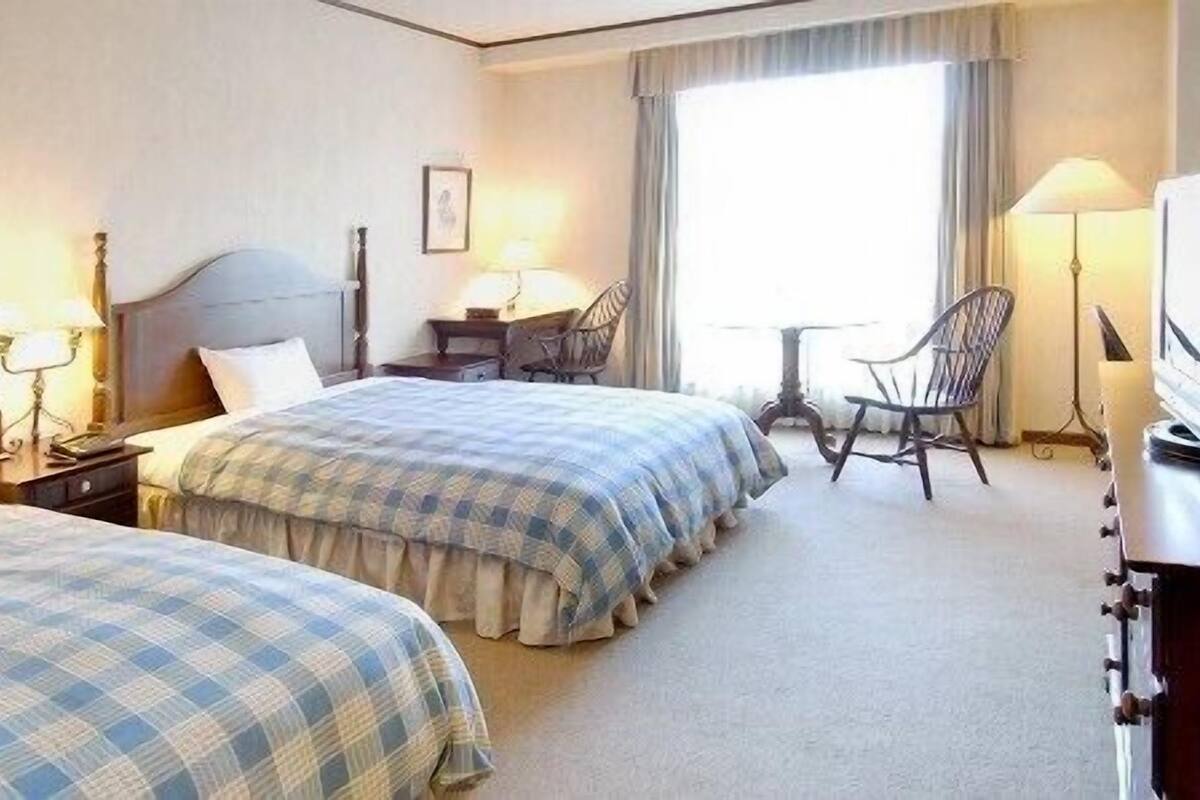 Una habitación de hotel con dos camas, un escritorio, una silla, una lámpara y un televisor.