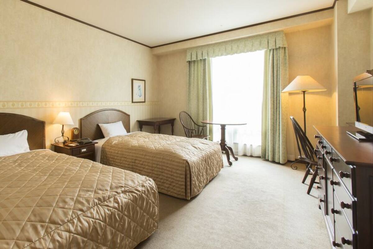 Una habitación de hotel con dos camas, un escritorio, una silla, una lámpara y un aparador.