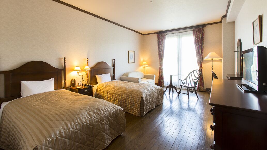 Quarto de hotel com duas camas, televisão, escrivaninha e uma cadeira.