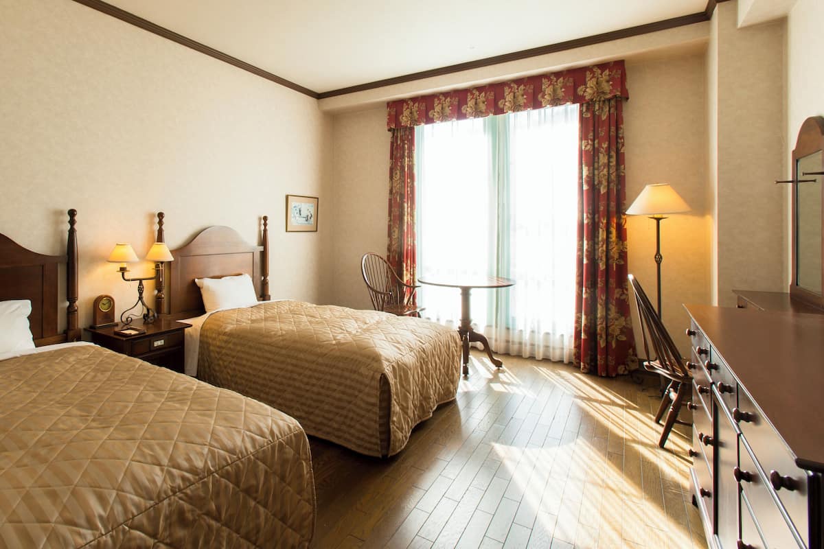 Ein Hotelzimmer mit zwei Betten, einem Nachttisch mit Lampen, einem Sessel, einem kleinen Tisch und einer Kommode.
