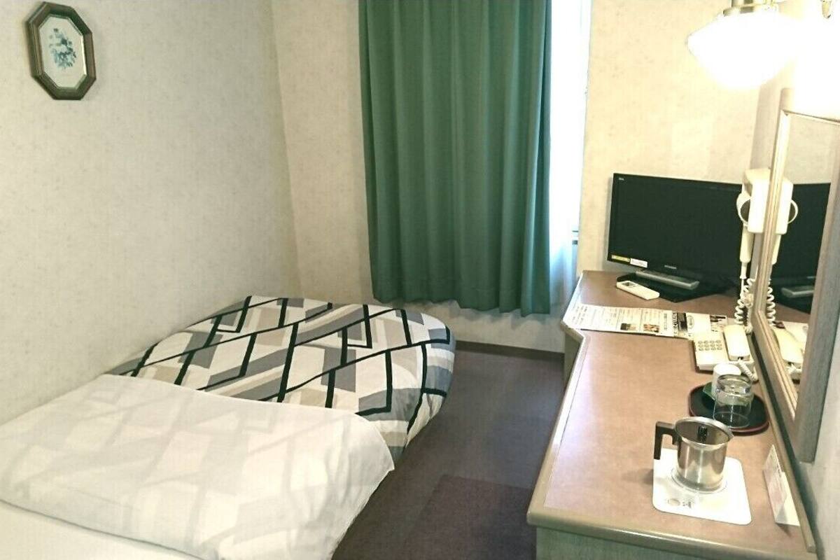 A hotel room with a bed, a desk with a telephone, a television, and a window with curtains.