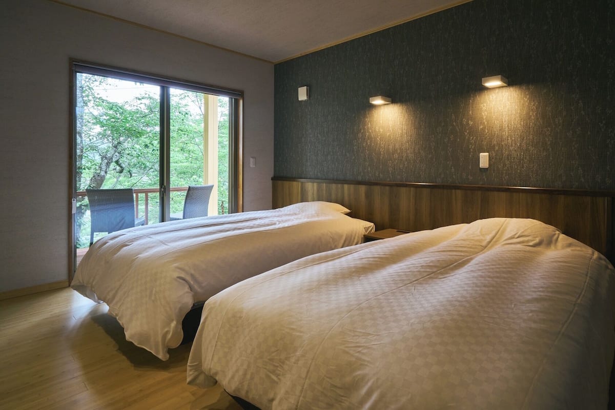 A bedroom with two beds, a large window, and a view of trees.