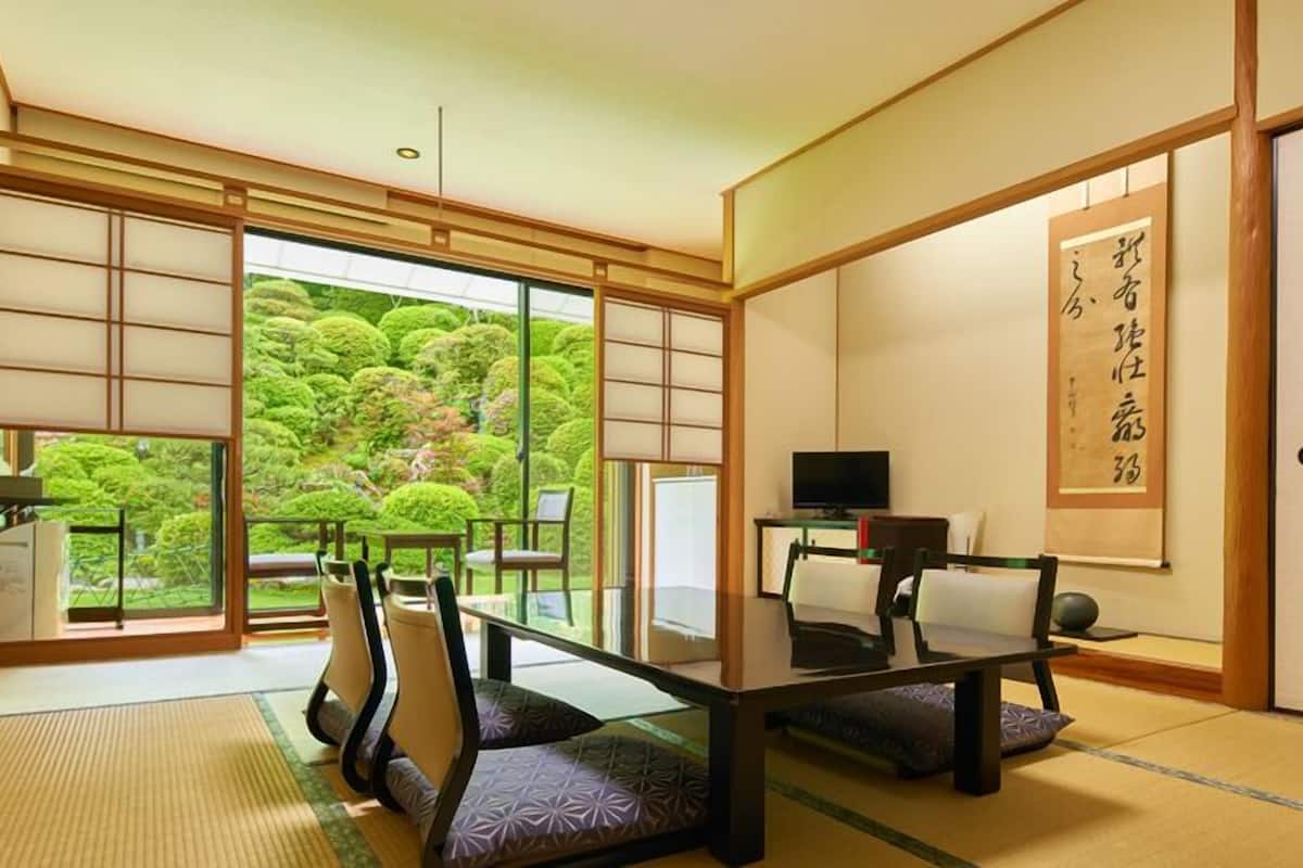 Perinteinen japanilainen huone, jossa on tatamimatto, matala pöytä, tuoleja, televisio ja suuri ikkuna, josta avautuu näkymä vehreään puutarhaan.