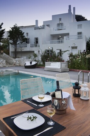 A poolside dining setup with a table, chairs, and a bottle of champagne. - Nefeli hotel (Skiros)