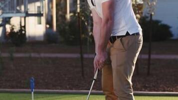 A person on a golf course with a putting green, a flagstick, and a golf ball.