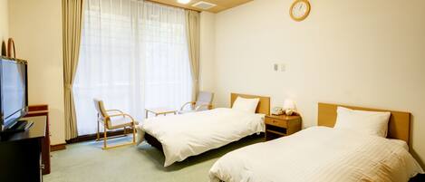 Ein Hotelzimmer mit zwei Betten, einem Fernseher, einem Sessel und einem Fenster mit Vorhängen.