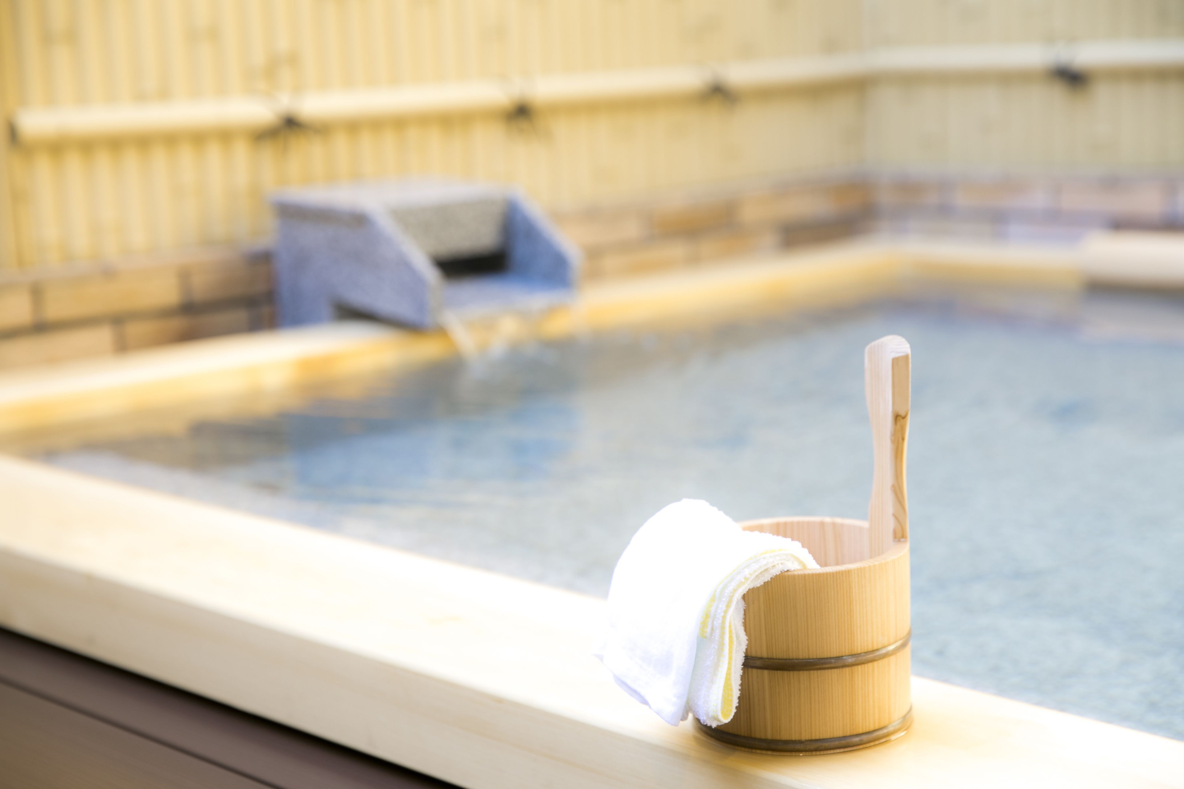 A wooden bucket with a towel and a wooden ladle on a poolside.