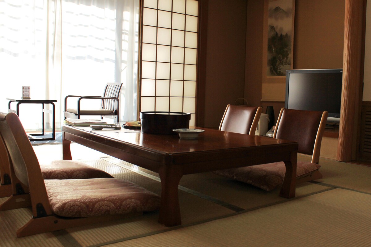A traditional Japanese room with tatami flooring, a low table, and two chairs.