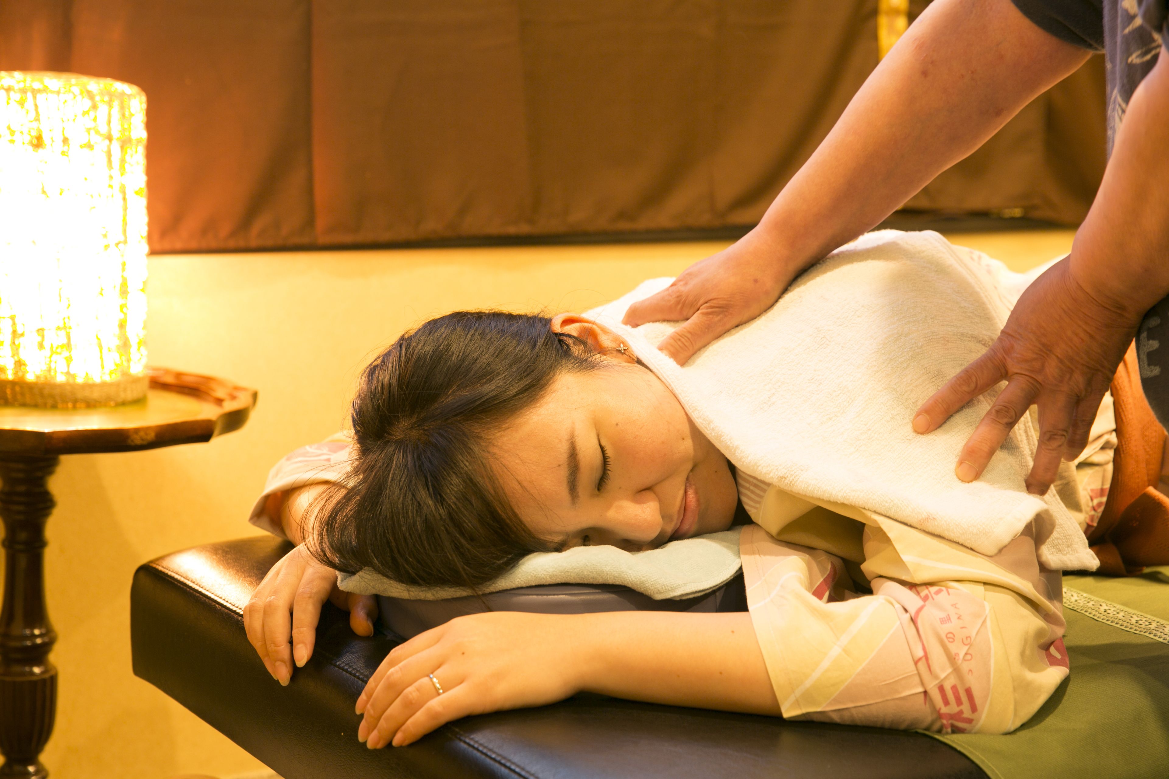 A person receiving a massage on a massage table with a lamp in the background.