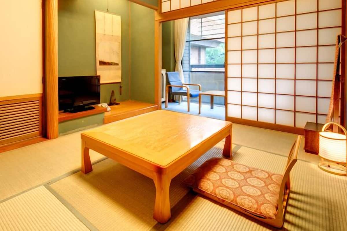 Una habitación japonesa tradicional con suelo de tatami, una mesa de madera baja, un televisor y puertas correderas.