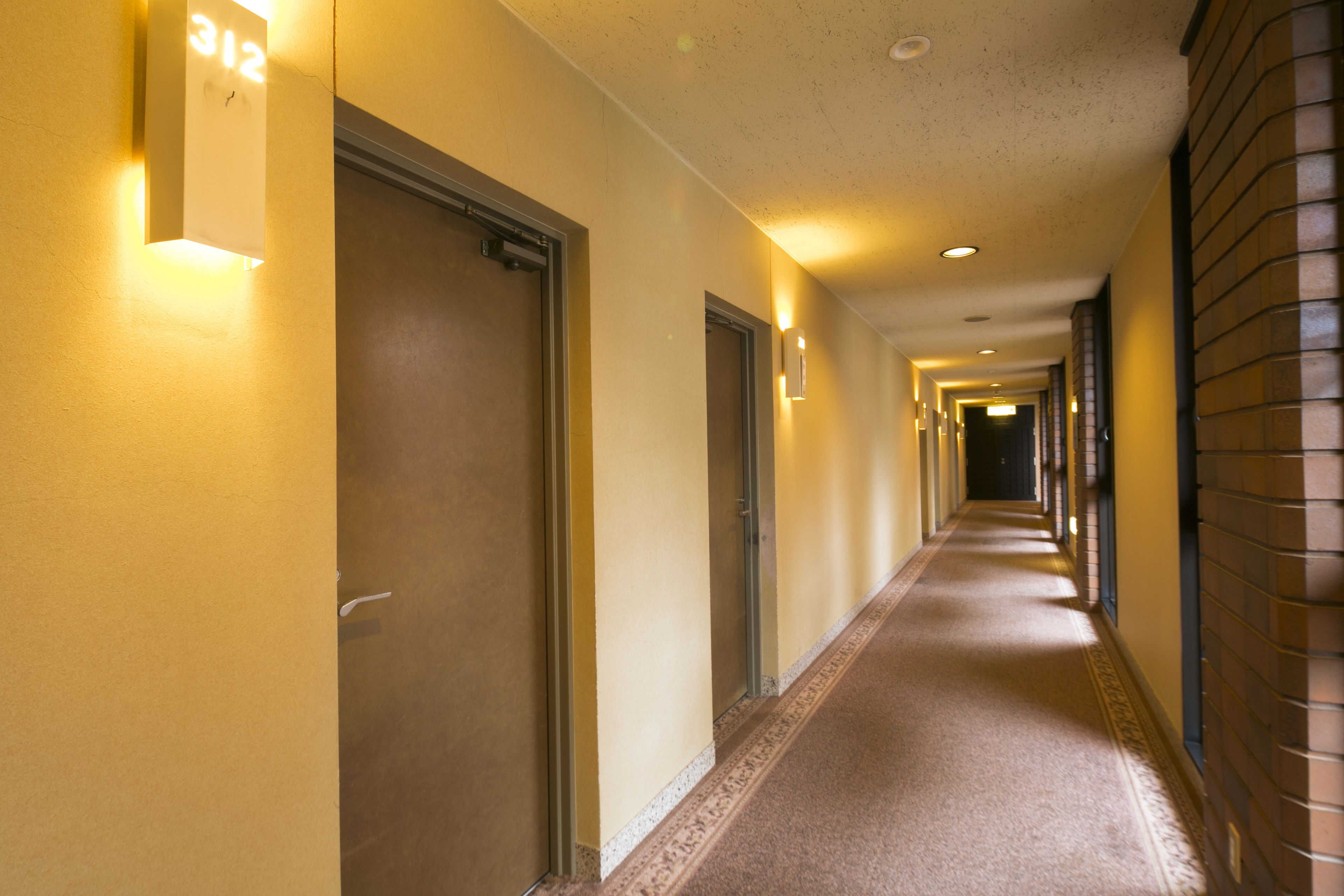 Un couloir d’hôtel avec des portes numérotées 312, 313 et 314, et un mur de briques sur la droite.
