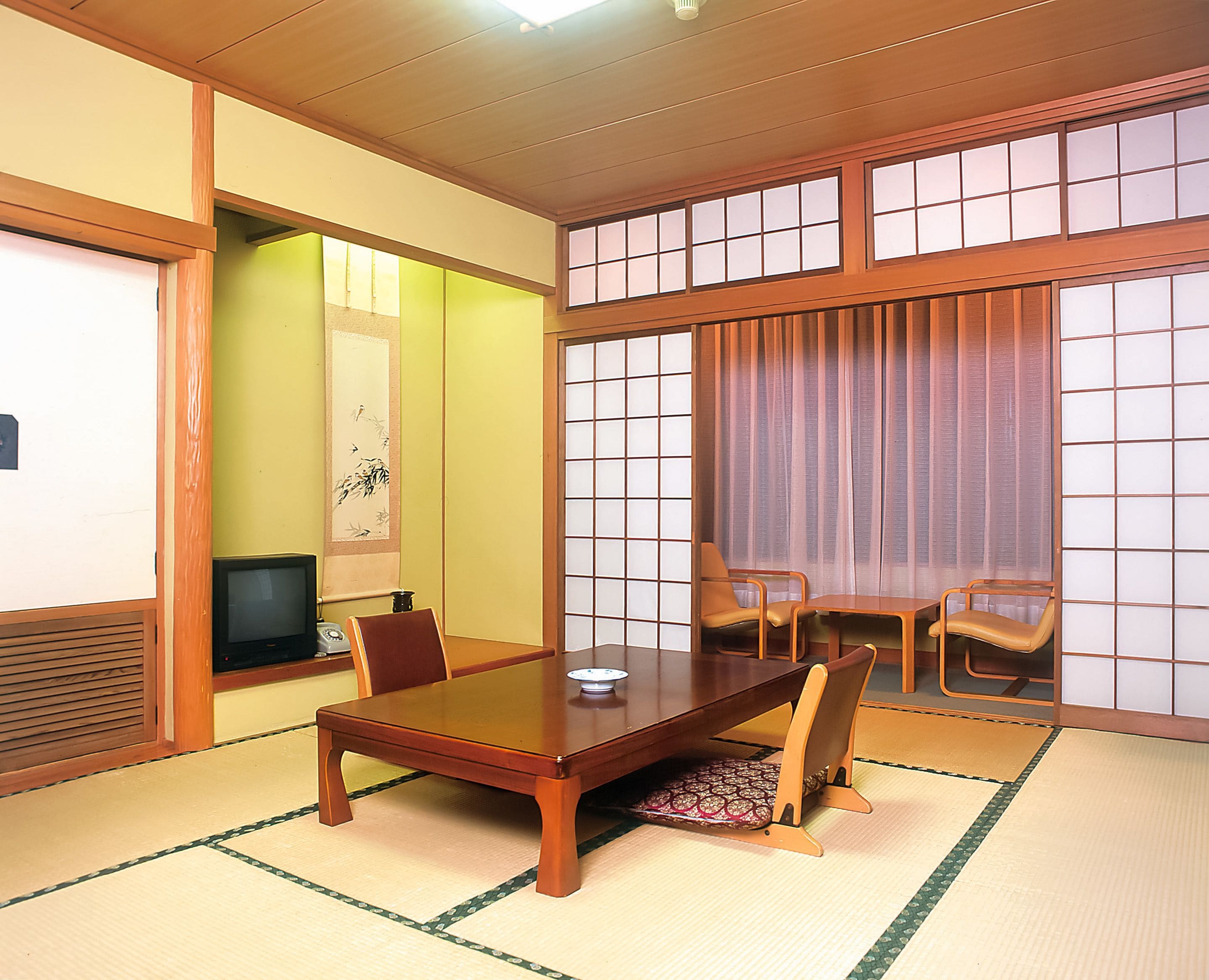 A traditional Japanese room with tatami flooring, a low wooden table, and two chairs.