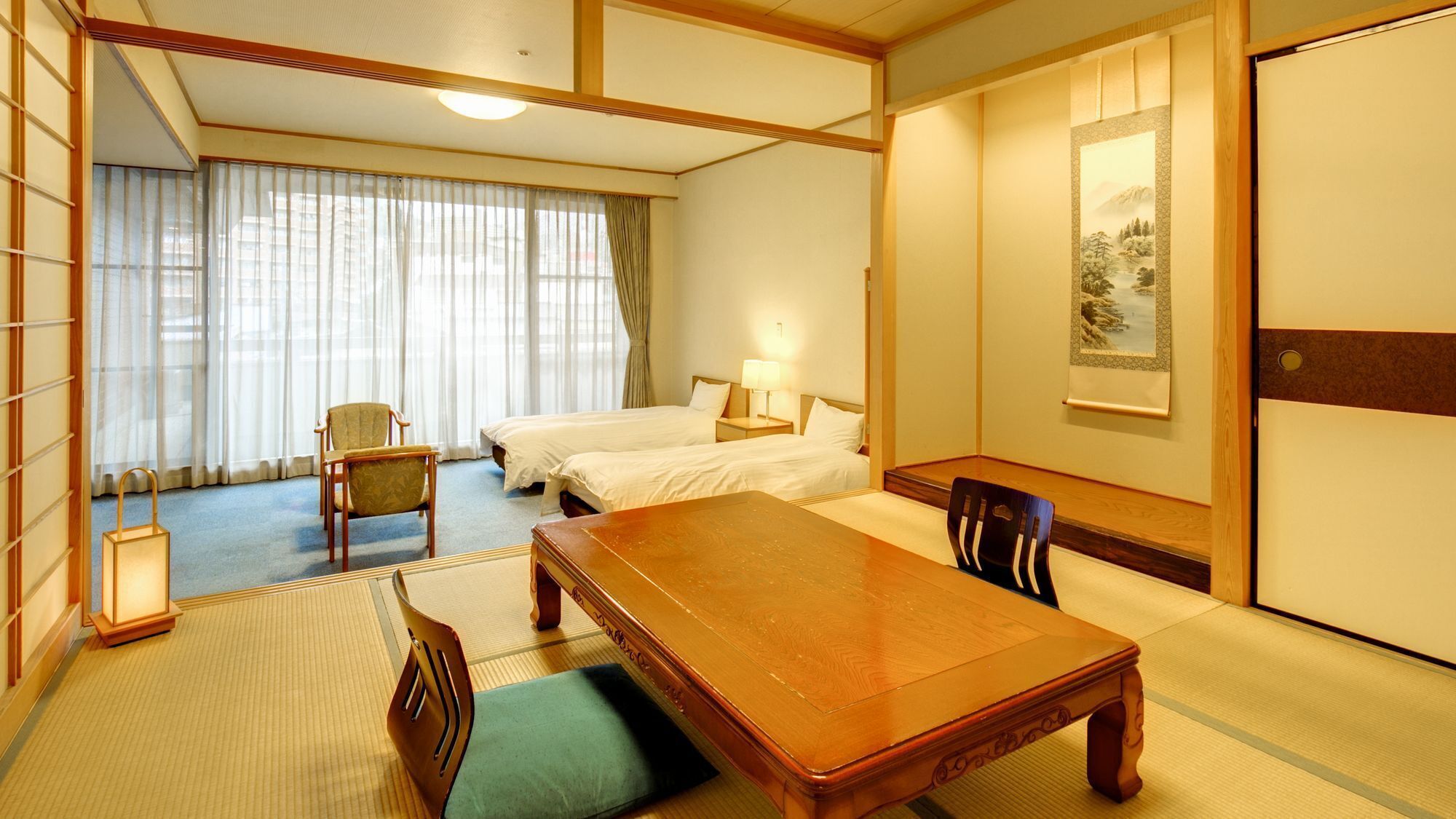 Habitació d'hotel de planta tradicional japonesa, amb tatami, dos llits, taula de fusta i porta corredissa.