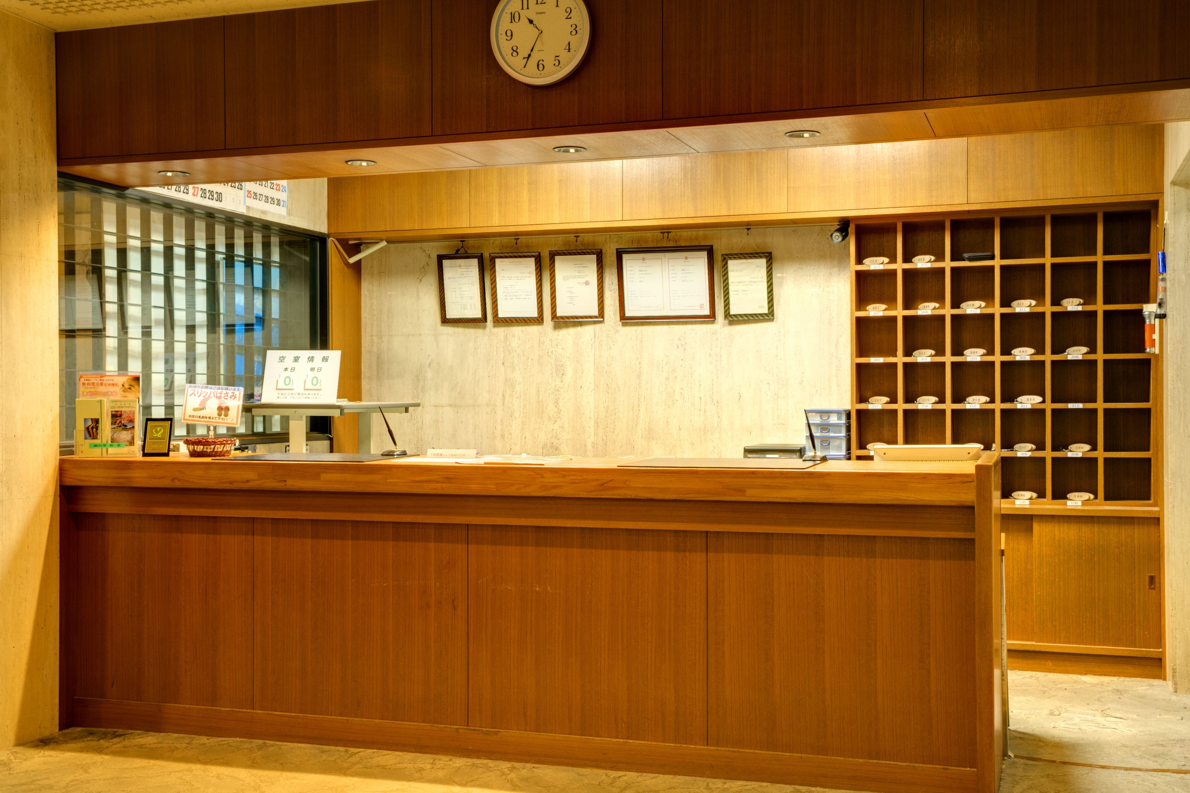 A reception desk with a wooden finish, a clock above it, and a wall with framed documents.