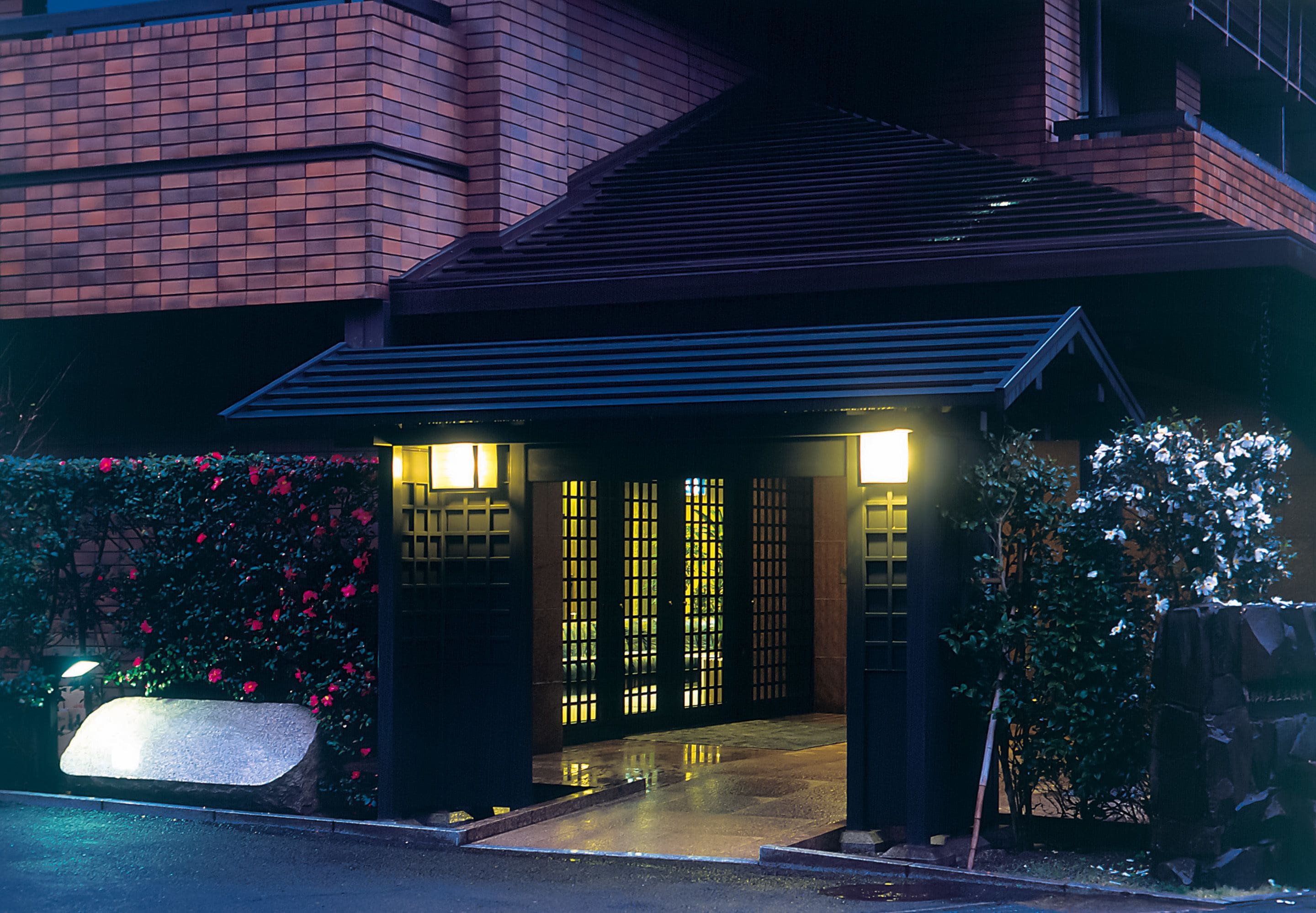 A modern building with a brick facade, a dark entrance with illuminated panels, and a stone bench in the foreground.