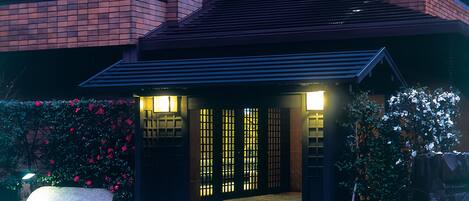 A modern building with a brick facade, a dark entrance with illuminated panels, and a stone bench in the foreground.