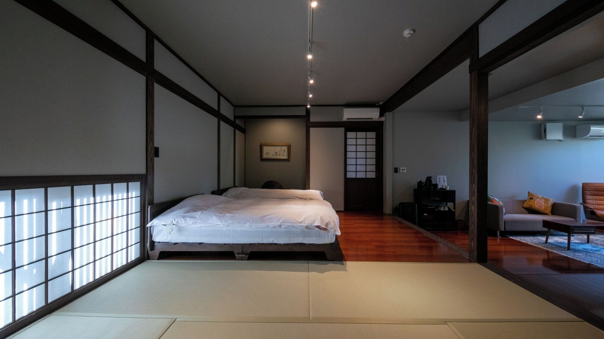 A traditional Japanese-style room with tatami flooring, a bed, a sliding door, and a view of a balcony.