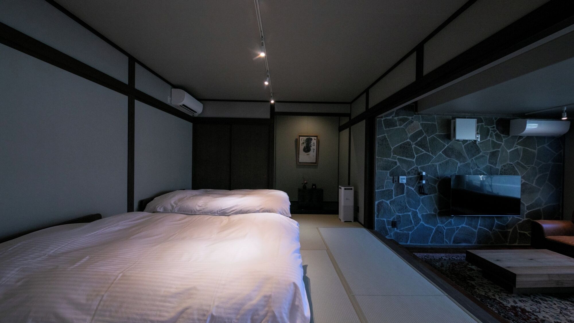 A modern bedroom with a bed, a stone wall, and a mounted TV.