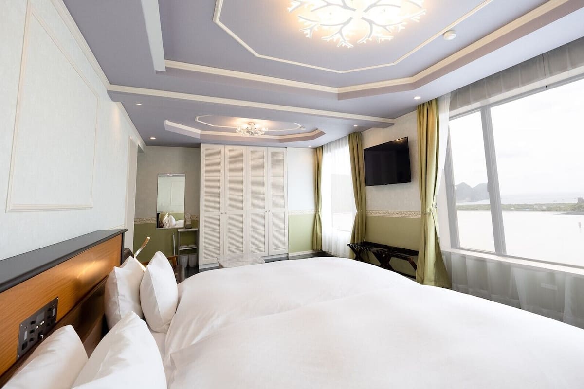 A hotel room with a large bed, a TV mounted on the wall, a wardrobe, and a view of the sea.