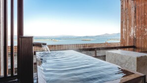 A hot spring bath with a wooden deck and a view of the sea and mountains.