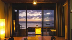 A dining area with a view of the sea, a wooden table, chairs, and a candlelit table lamp.