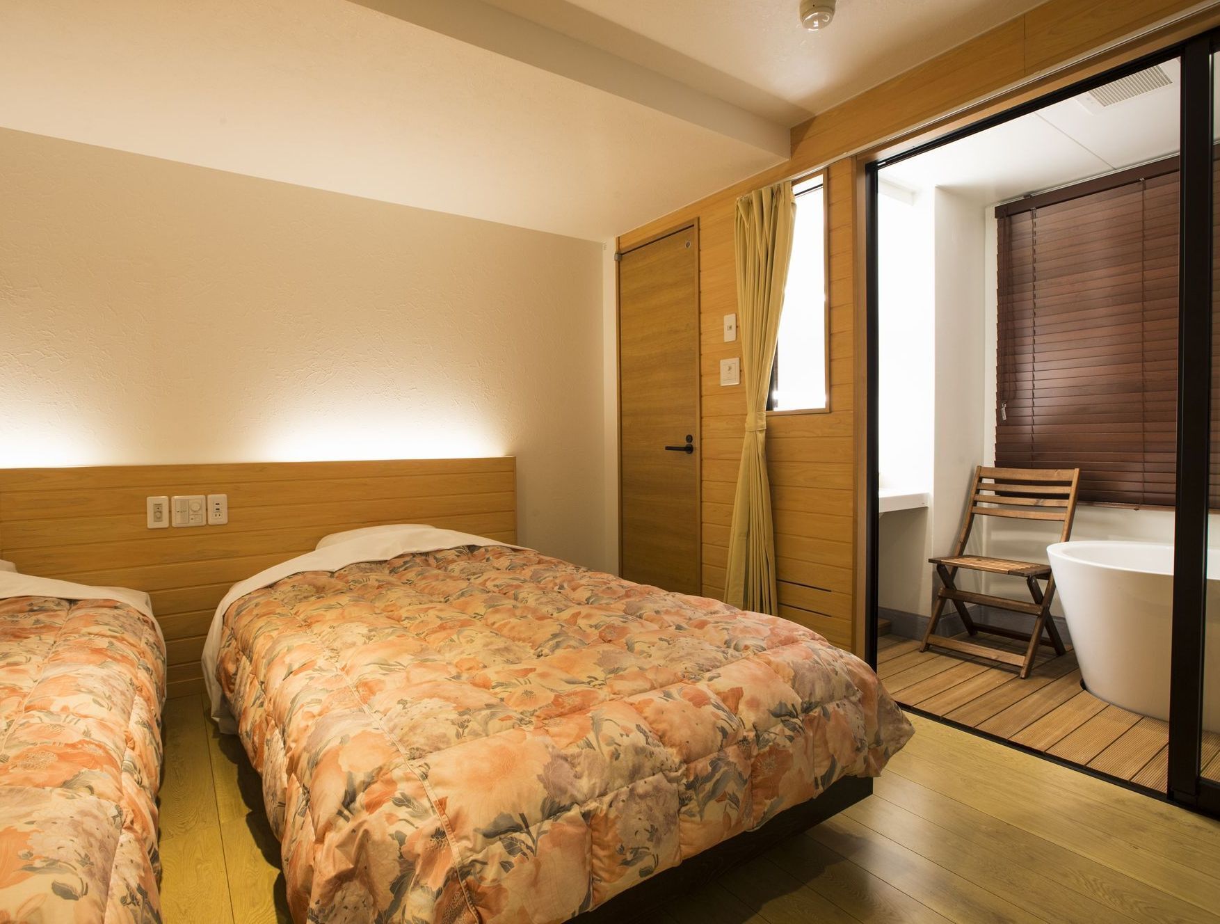 Une chambre avec deux lits, une tête de lit en bois, une fenêtre avec des rideaux, une chaise en bois et une baignoire.