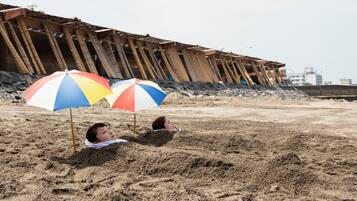 Una persona acostada en la arena con dos sombrillas de playa.