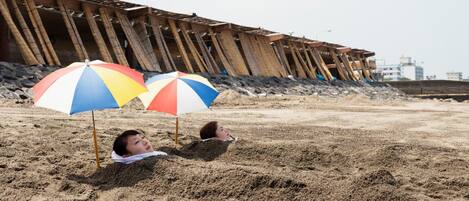A person lying in the sand with two beach umbrellas.