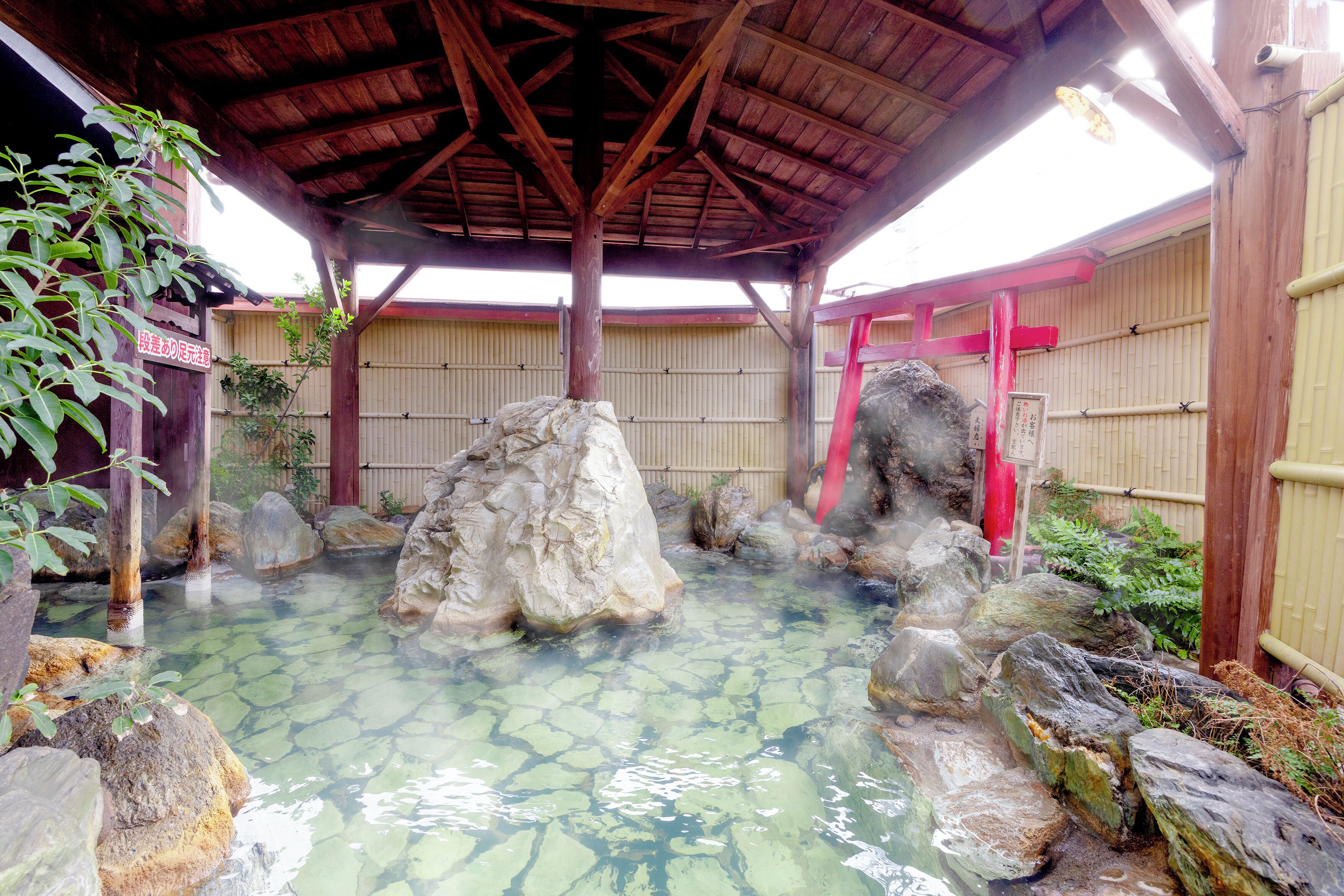 A traditional Japanese hot spring with clear water, large rocks, and a wooden roof structure.
